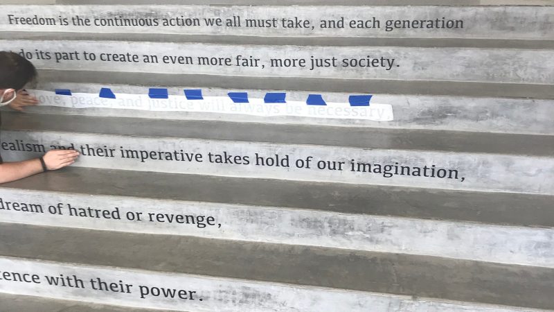  A masked Moss Arts Center graduate assistant helps to install a quote from John Lewis on the risers of the steps from the Grand Lobby to the Francis T. Eck Exhibition Corridor