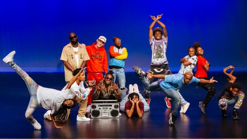  The cast of "Memphis Jookin': The Show" pose on stage with a boombox. The background is lit by blue light.