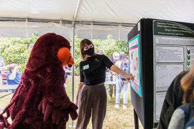 A student points to their scientific research poster and presents their findings to the HokieBird.