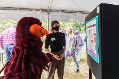 A student looks towards their scientific research poster and presents their findings to the HokieBird.