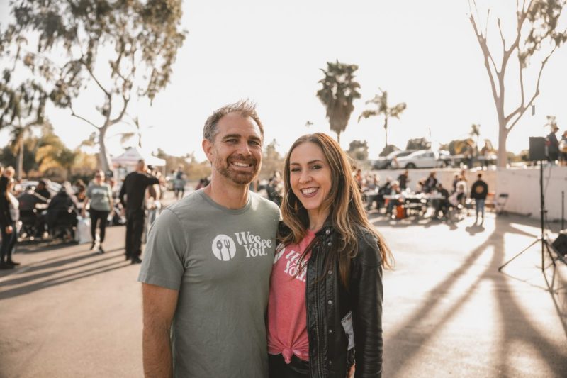 Kevin and Laura Cieslukowski pose for a photo with blurred people walking and mingling in the background.