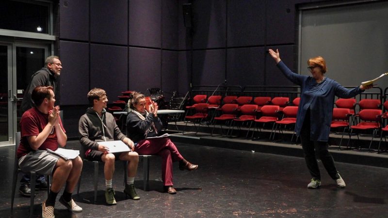 Patty Raun poses triumphantly while other cast members clap.