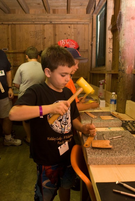 A young boy with a mallet and brass leatherworking tool.