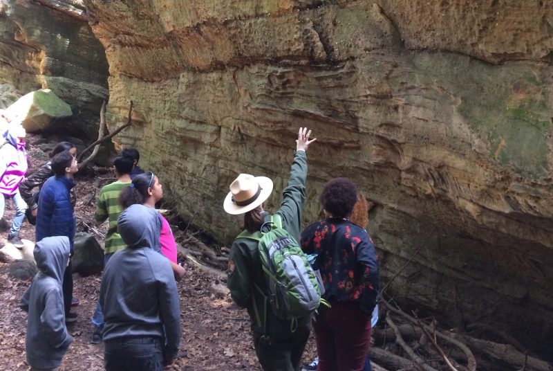 Park ranger pointing out features on a rock wall to a group of children.