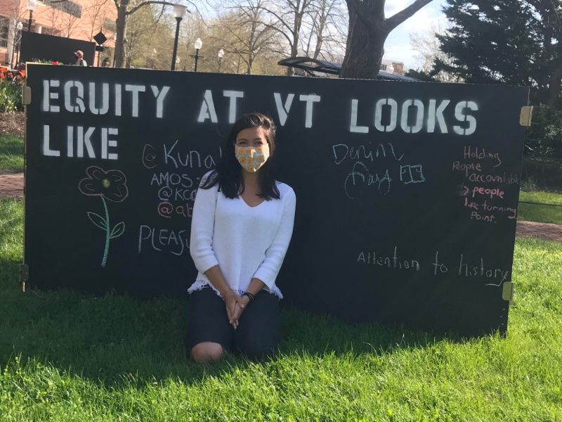 Malia Pownell wearing a mask and kneeling in front of one of her project boards