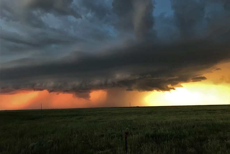 A prairie landscape at dusk, with large clouds and a tornado at the center.