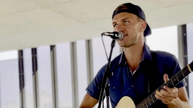 Blake Robert sings into a microphone while playing the guitar.