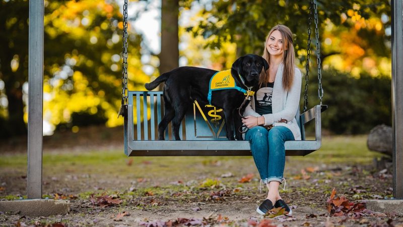 Woman and black dog sitting on a swing.