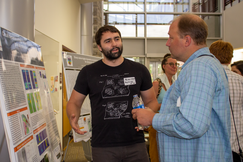 This image shows Kaiser Arndt standing next to a research poster and speaking to Christopher Thompson.